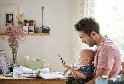 Man with laptop and papers looking at playful son